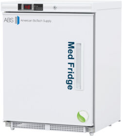 A white ADA-compliant under-counter medical refrigerator with ABS American BioTech Supply and Med Fridge printed on the front. It has a digital temperature display on the top, a vertical handle, and a green leaf logo in the lower right corner. The door opens from the left