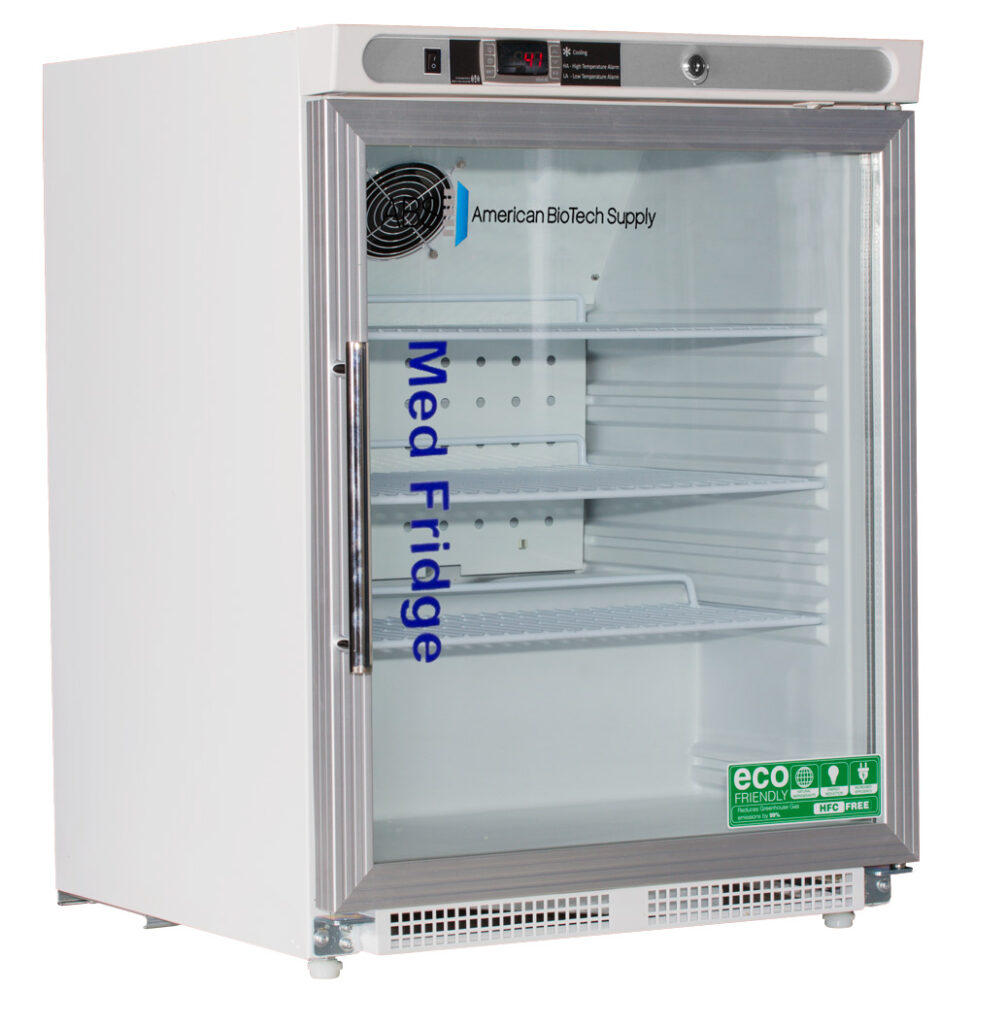 A small, white compact pharmacy fridge with a glass door, labeled Med Fridge and American BioTech Supply. Inside are three adjustable shelves. A digital display sits above the door, and eco-friendly, energy-efficient stickers are on the lower right.