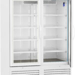 A large, white commercial refrigerator with glass double doors, interior shelves, and a digital temperature display at the top. The fridge sits on wheels and has ventilation grilles at the bottom, showing it is empty and clean inside.