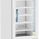 A tall, white medical refrigerator with a glass door, labeled “MedFridge.” It has five metal shelves, a digital temperature display at the top reading 4.0°C, wheels on the base, and one small blue and white bottle stored on the upper right shelf.