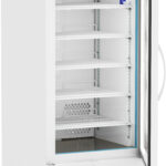 A tall, white laboratory refrigerator with a glass door stands open, revealing five empty wire shelves. The digital display at the top reads 4.0°C. A single small vial sits on the top shelf. The fridge is on wheels and has ventilation grilles at the bottom.