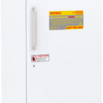 A tall, white upright freezer with a vertical handle on the left side. It has yellow and red warning labels on the front door and a digital temperature display at the bottom. The freezer is from American BioTech Supply.