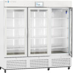A large, white, commercial refrigerator with three glass doors, interior shelves, and a digital temperature display showing 4.0°C. The unit has metal handles, vents at the bottom, and bright interior lighting, with all shelves currently empty.