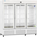 A large, white, three-door commercial refrigerator with glass doors showing empty adjustable shelves inside, vents at the bottom, wheels for mobility, and a digital display at the top center. The doors have vertical handles and the interior is brightly lit.