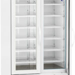 A large, white, double-door laboratory refrigerator with glass doors, multiple adjustable wire shelves, a digital temperature display on top, ventilation grilles at the bottom, and four caster wheels for mobility. The fridge interior is empty.