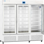 A large, white, commercial refrigerator with three glass doors and metal handles, standing on wheels. The fridge is empty, with multiple white shelves inside each section and a digital control panel above the center door. Vents are visible at the bottom.