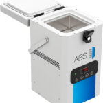 A white, box-shaped laboratory freezer with a digital display reading 6.5°C, labeled “ABS.” The lid is open, revealing a metal interior. The front panel has buttons and indicator lights, and the side features a handle and ventilation holes.
