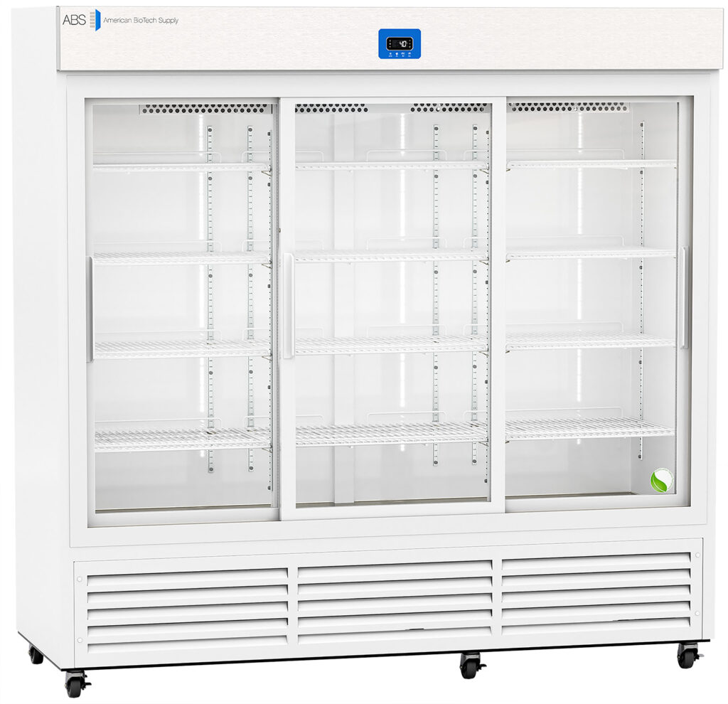 A large, commercial white refrigerator with three sliding glass doors and multiple empty wire shelves. A digital temperature display is above the center door. Only one green tennis ball sits on the bottom right shelf; the rest of the shelves are empty.