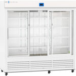 Large, white commercial refrigerator with three sliding glass doors and multiple adjustable wire shelves inside. The unit has ventilation grilles at the bottom, a digital display at the top center, and is empty with a clean, modern design.