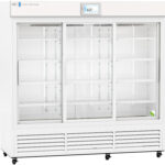 A large, white, commercial refrigerator with three clear sliding doors and empty wire shelves inside. A digital display above shows the temperature as 4.0°C. Only one small green and white object sits on the lower shelf on the right side.