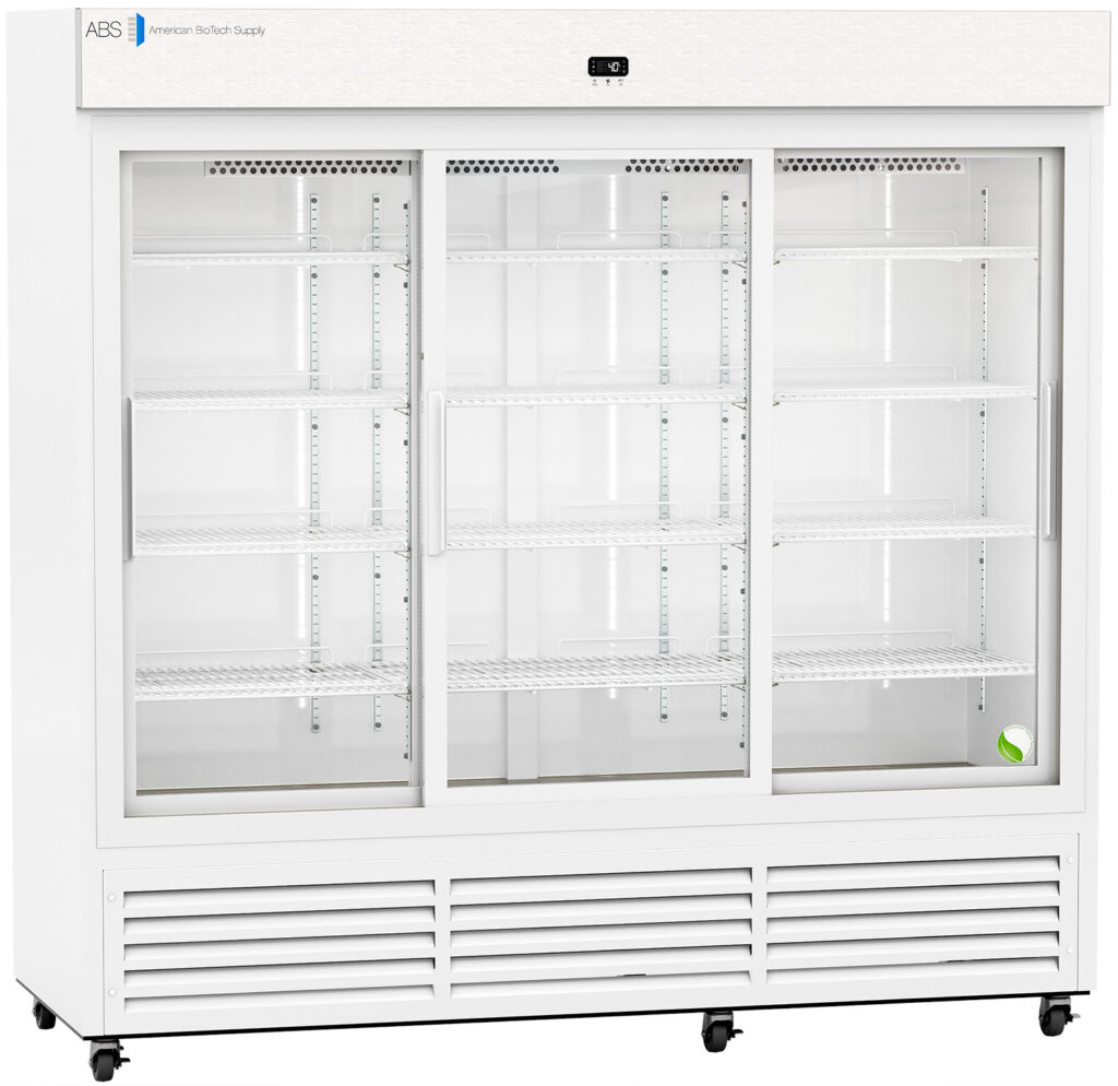 A large, white commercial refrigerator with three glass sliding doors, empty wire shelves inside, and vents along the bottom. A single green and white tennis ball sits on the bottom right shelf. The unit is well-lit and on wheels.