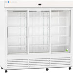 A large, white commercial refrigerator with three glass sliding doors, empty wire shelves inside, and vents along the bottom. A single green and white tennis ball sits on the bottom right shelf. The unit is well-lit and on wheels.