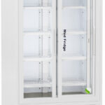 A tall, white medical refrigerator with glass double doors showing empty wire shelves inside. The control panel is above the doors, and the bottom has a vent. The label reads Med Fridge and American Biotech Supply. The fridge is on caster wheels.