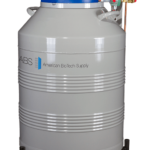 A large silver liquid nitrogen storage tank labeled American BioTech Supply with a blue lid, digital control panel, and attached pipes, standing on a wheeled base against a plain white background.