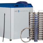 A large white and blue laboratory freezer labeled “ABS American BioTech Supply” stands on wheels. In front are two coiled hoses and three tall racks holding multiple clear, rectangular sample containers. A folded cloth sits on top of the freezer.