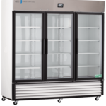 A large, three-door commercial refrigerator with glass doors, white exterior, multiple adjustable shelves, digital temperature display, vents at the bottom, and casters for mobility. The interior is empty and well-lit.