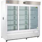 A large, commercial white refrigerator with three clear glass sliding doors, empty interior shelves, a digital display above, and a stainless steel upper panel. The unit stands on small wheels and has ventilation grilles at the bottom.