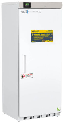 A tall, white American BioTech Supply refrigerator stands upright. Its door displays yellow warning labels about flammable material storage and fire risk, plus a caution sign. A small digital control panel is located at the top left above the door.