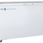A large, white chest freezer with the logo “ABS American BioTech Supply” on the front. It has a flat lid, a small digital control panel at the bottom right, wheels for mobility, and a round green sticker on the top right corner.