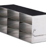 A rectangular metal box with a shiny finish, divided into six equal open compartments in two vertical rows of three; it has a handle on the right side and a latch on the left, suggesting it is used for organized storage or carrying items.