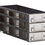 A metal storage unit with three pull-out drawers, each featuring large rectangular handles. The unit is rectangular, silver with black accents, and has an industrial design. The drawers are partially open, revealing horizontal dividers inside.