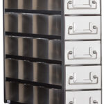 A metal storage unit with five large, white drawers stacked vertically on the right and three rows of open, horizontal metal compartments on the left. Each drawer has a large silver handle. The unit has a modern, industrial design.