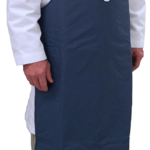 A person wearing a white lab coat, a patterned tie, and beige pants models a long, dark blue protective apron with a round blue and white logo on the chest. The apron covers the torso down to the ankles. The background is plain white.