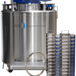 A large, stainless steel cryogenic storage tank with a digital display on top and the logo ABS American BioTech Supply on the side. In front of the tank are two tall racks with multiple blue-capped storage boxes and a metal circular component on the floor.