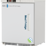 A ADA-compliant white medical refrigerator by American BioTech Supply with a digital display, labeled Med Fridge on the left hinged solid door. It features a vertical handle and an NSF/ANSI certification sticker in the lower right corner. The fridge sits on metal legs.