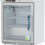 A white medical ADA-compliant refrigerator with a glass door showing three adjustable shelves inside. The door displays the words Med Fridge and American BioTech Supply. A digital control panel is at the top, and an NSF/ANSI 456 certification sticker is on the bottom right of this left hinged door model.