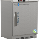 A stainless steel medical vaccine refrigerator labeled Med Fridge with a digital display and control panel on top. The right hinged door has a sturdy handle, and the lower right corner features an NSF/ANSI 456 certification logo. The brand American BioTech Supply is visible.