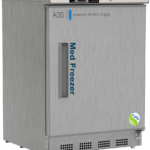 A stainless steel NSF/ANSI 456 certified medical vaccine freezer labeled Med Freezer by American BioTech Supply, with a digital temperature display on top showing -20°C, a handle on the left, a vent at the bottom, and a certification sticker on the lower right corner.