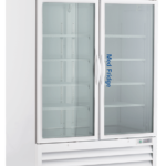A large, white Pharmacy refrigerator with glass double doors, labeled Med Fridge. The fridge has several empty shelves inside, ventilation grilles at the bottom, and stands on wheels for mobility. The doors have vertical handles in the center.